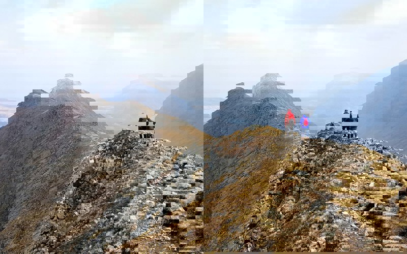 Two people hiking on top of a grassy mountain