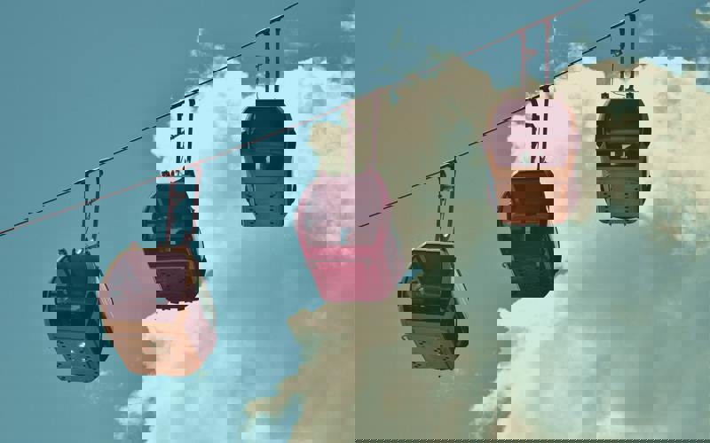 Three cable cars, two yellow and one red, hang against a backdrop of blue sky and white clouds. 