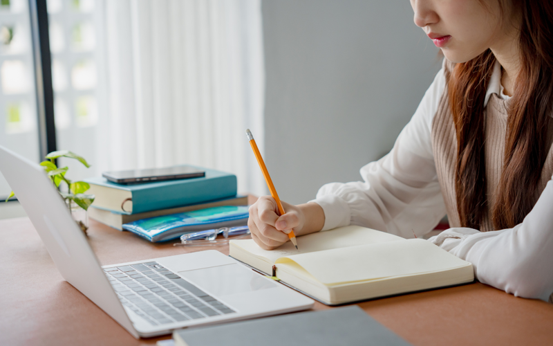 Woman using laptop and writing in a notepad.