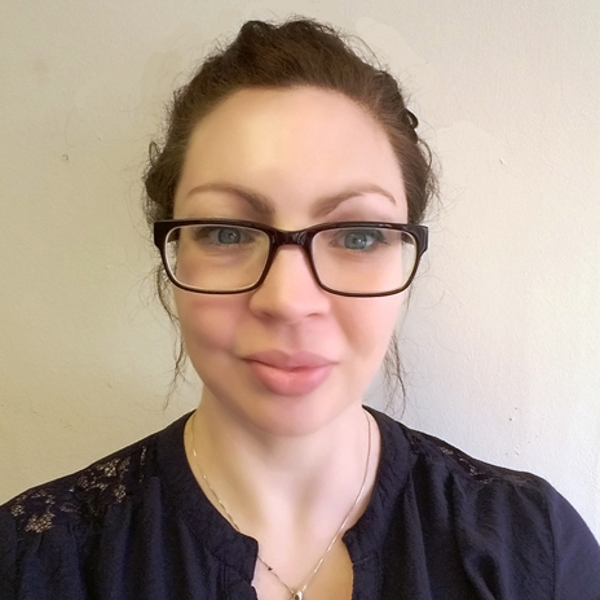 Headshot photograph of Christina Gilfedder. She is wearing dark glasses, a blue shirt, and smiles at the camera