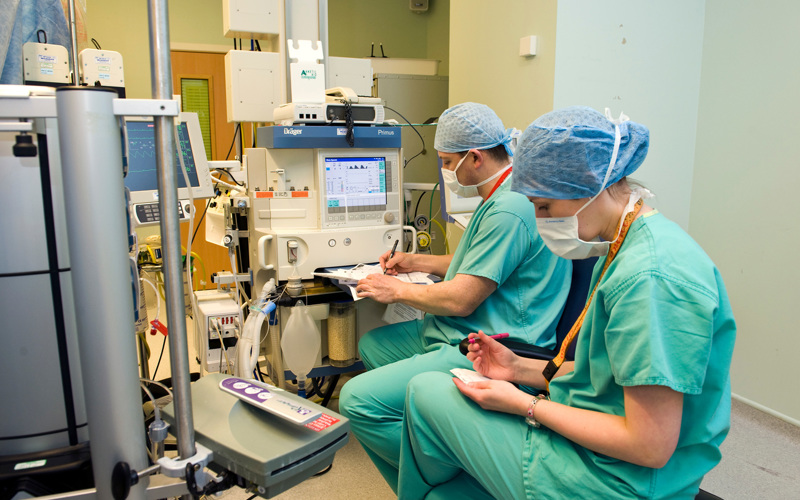 Two people in blue scrubs wearing masks work at hospital machinery