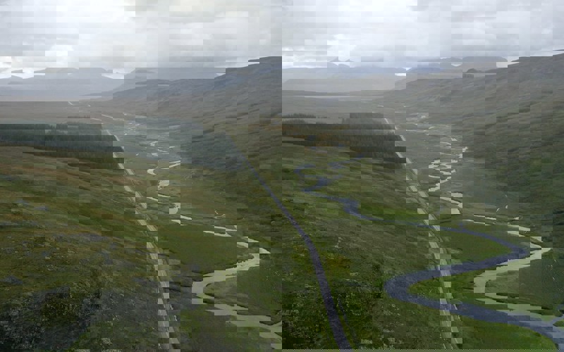 A winding river and straight road in a mountainous green valley