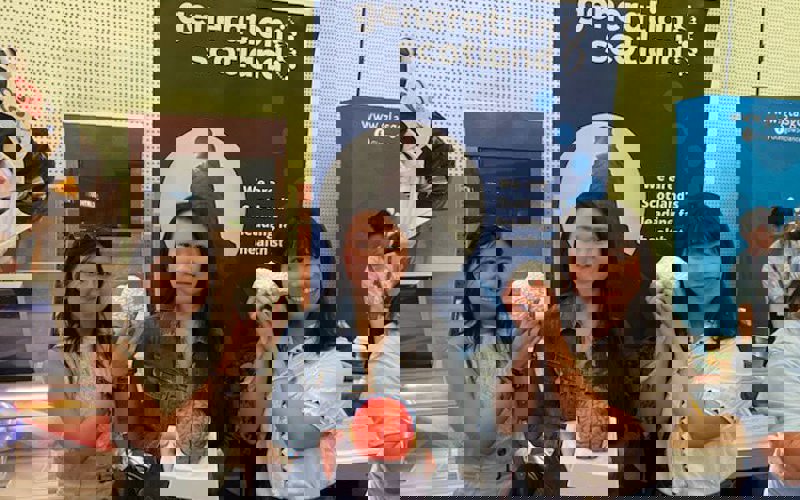 Three people hold models of brains. They are standing in front of a banner that reads 